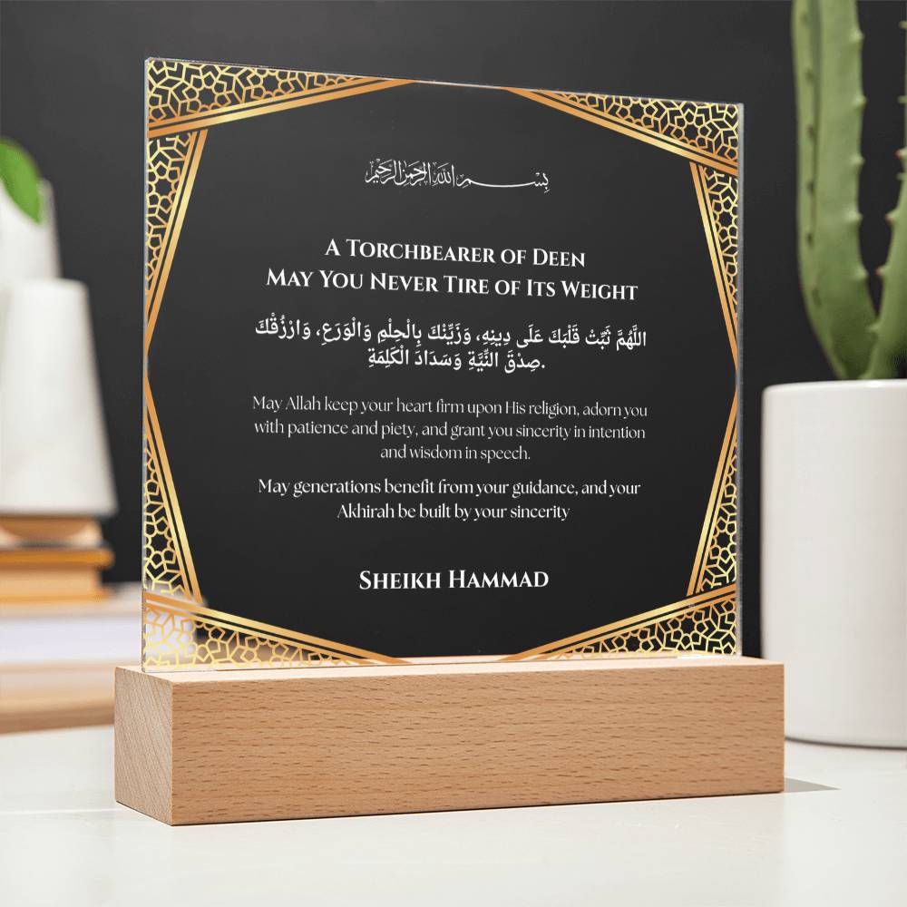 a framed prayer card with Arabic text, placed on a wooden stand.